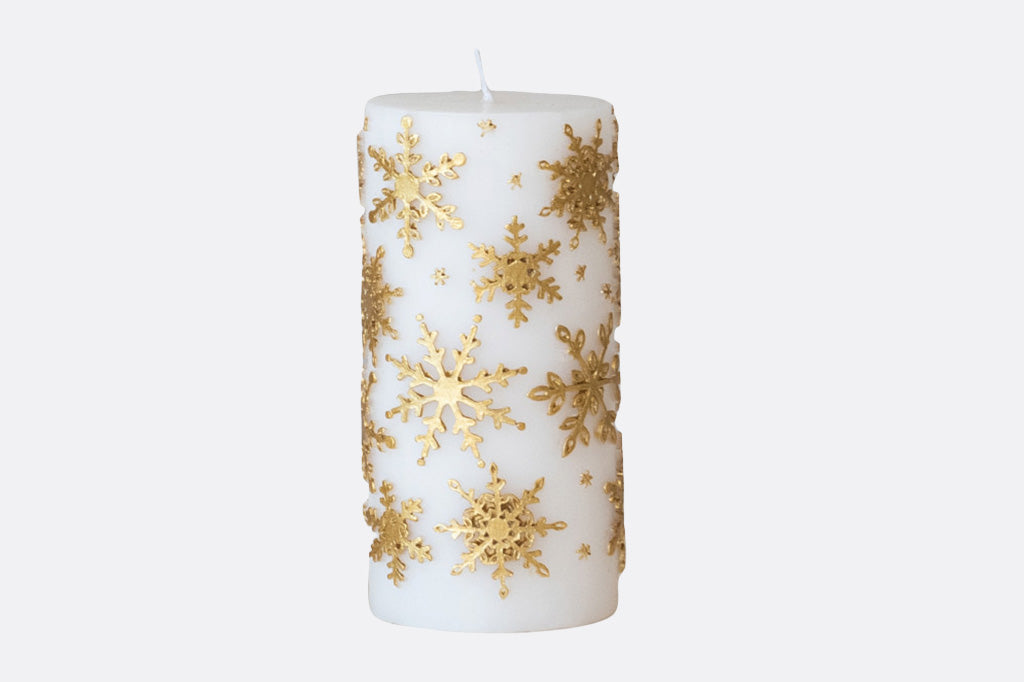 White candle with gold snowflake patterns on a white background