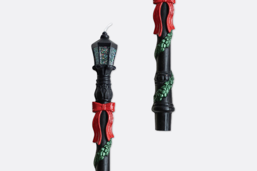 A close up of decorative candles of a lamp post with festive ribbons and greenery.