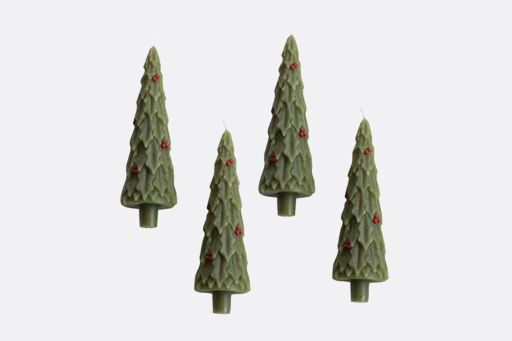 Four green Christmas tree-shaped candles with red berries on a white background