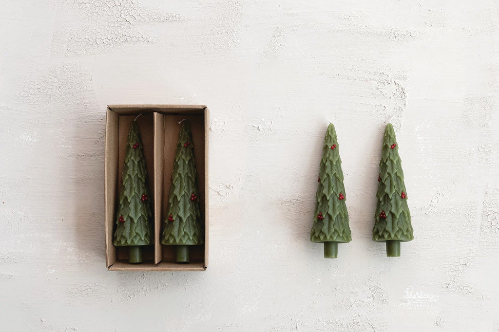 Green tree-shaped candles on a textured white surface, two shown in an open box.