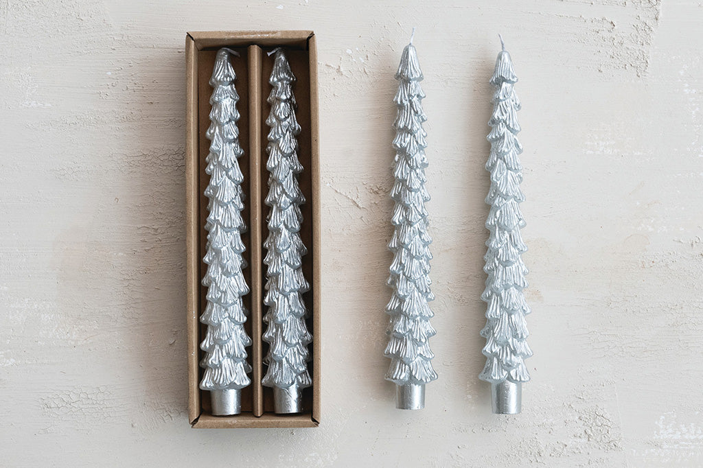 Two silver Christmas tree-shaped candles next to their packaging on a light background