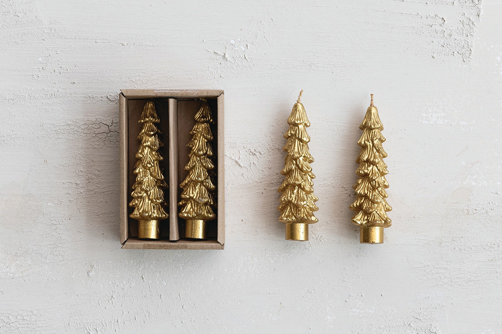 Four gold Christmas tree-shaped candles on a white textured surface shown near its box.