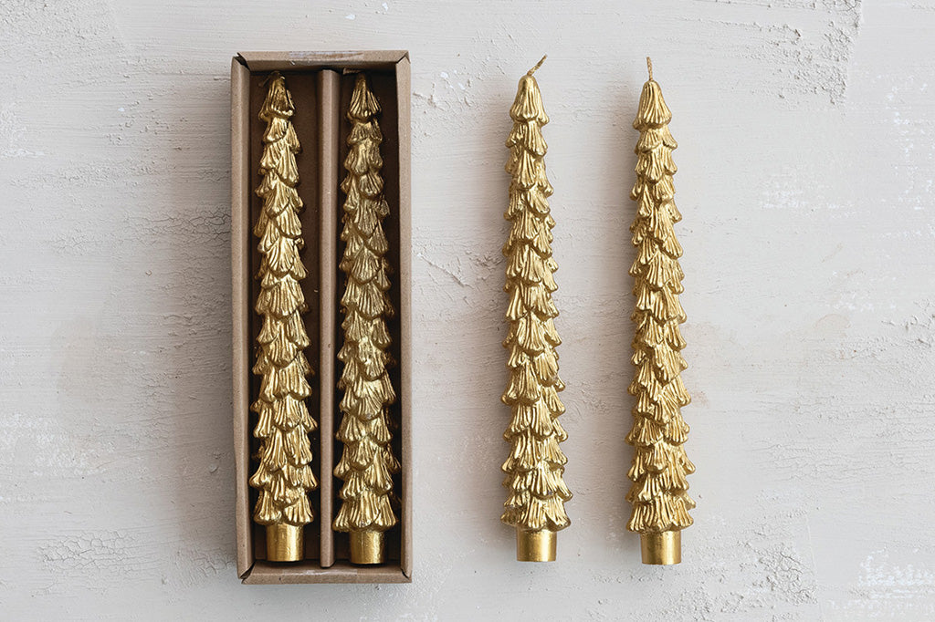 Four gold decorative tree shaped candles near its packaging