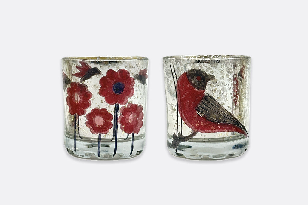 Two glass votive holders with floral and bird designs on a white background