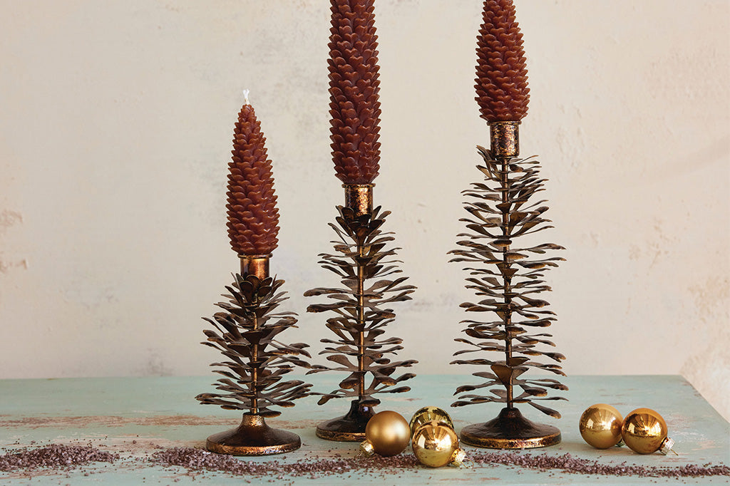 Decorative tree candleholders shown with pinecone candles on a holiday display