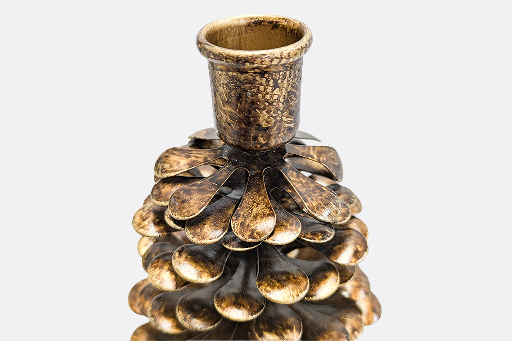 A close up of a metallic pinecone shaped candle holder on a white background