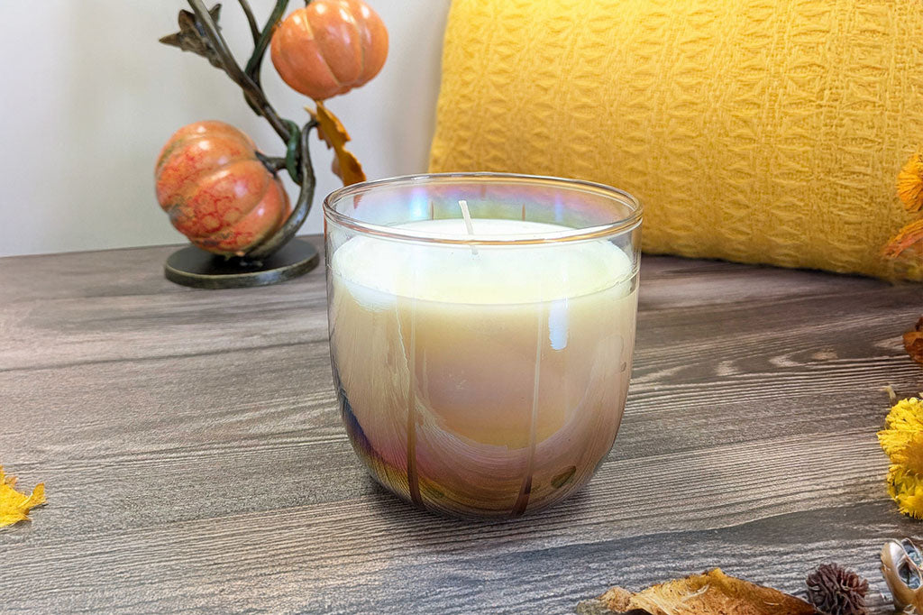 Candle in a glass jar with a decorative background featuring pumpkins and a yellow pillow.