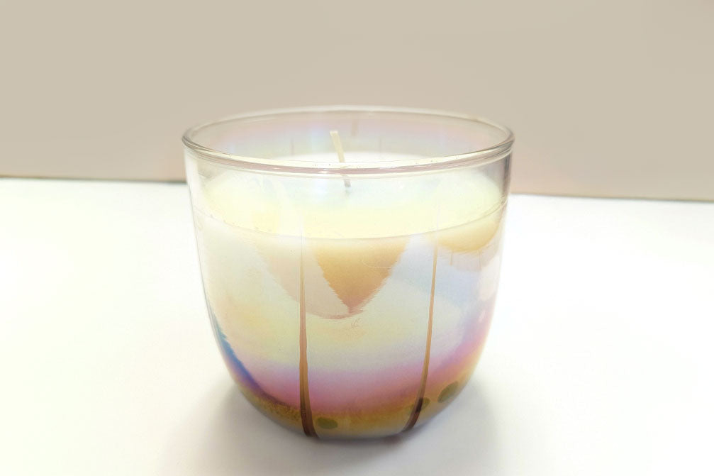 Iridescent glass candle on a white surface with a neutral background