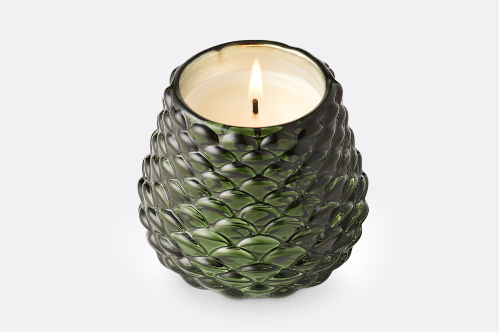 Green glass textured candle holder with a lit candle on a white background, pinecone texture