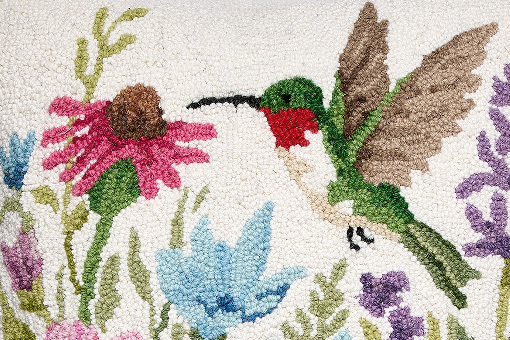 A hooked throw pillow featuring a green hummingbird and vibrant spring flowers.