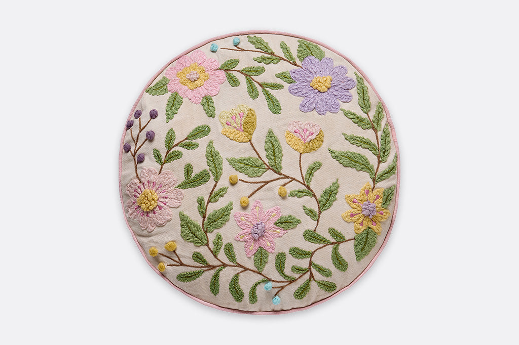 Round pillow with embroidered floral designs.