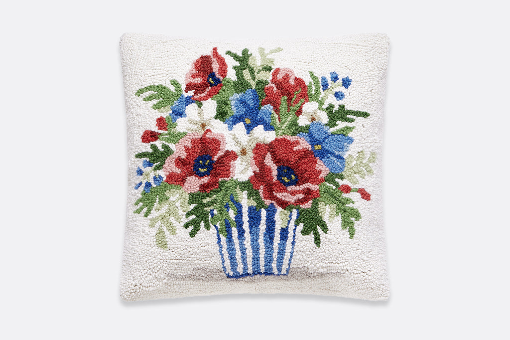 A hooked pillow of a bouquet of red, white, and blue flowers in a striped pot.