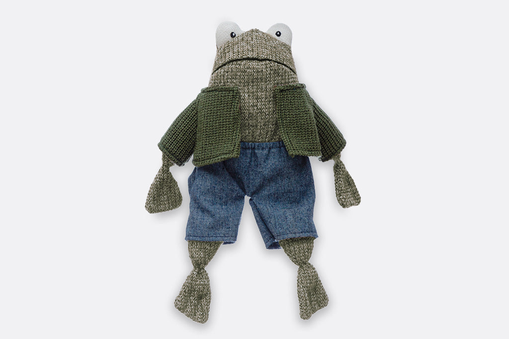 Frog stuffed animal wearing a green sweater and jean shorts.