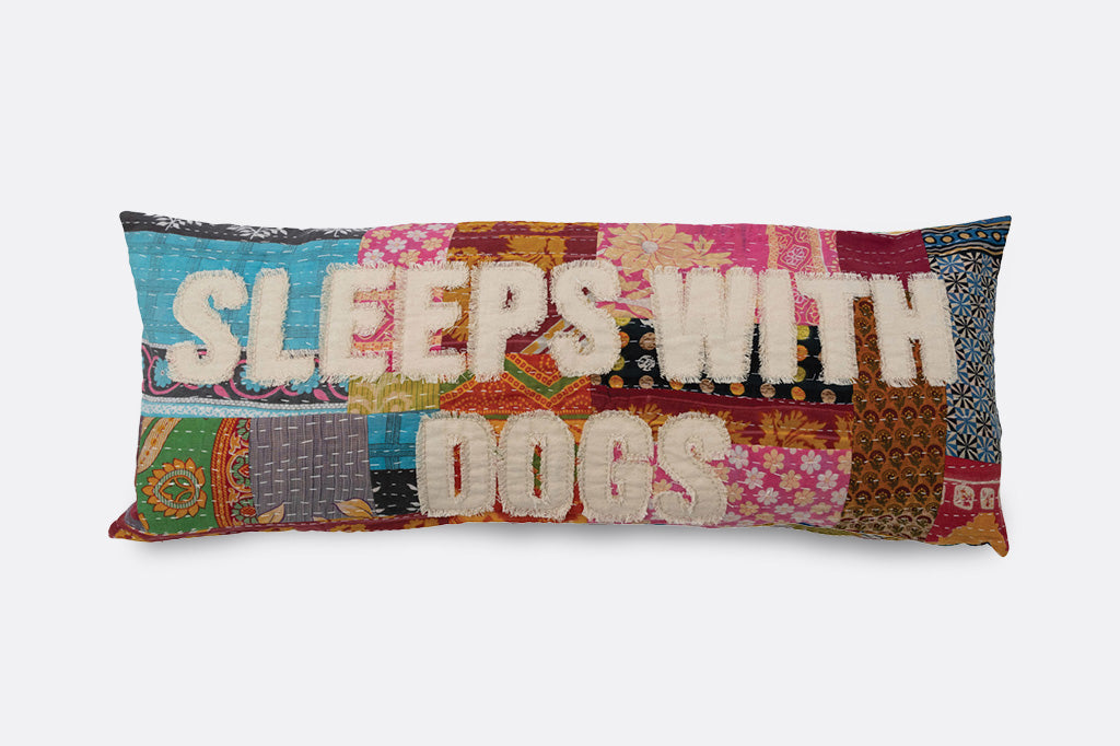 A patchwork pillow inscribed with the phrase "Sleeps with dogs."