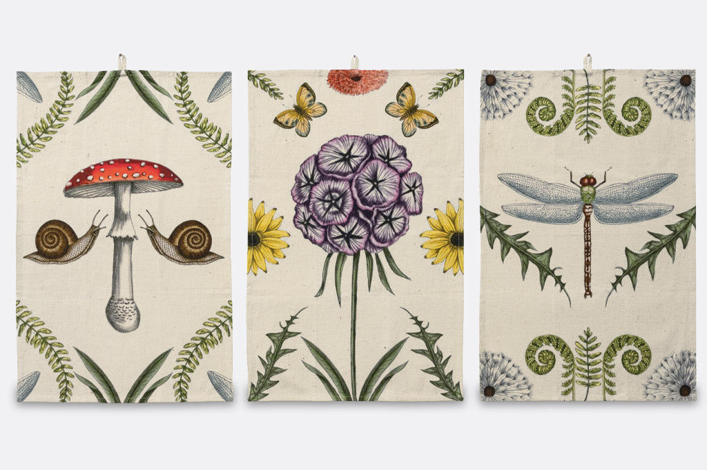A set of 3 dish towels that have illustrations of mushrooms, butterflies, flowers, snails, and dragonflies.