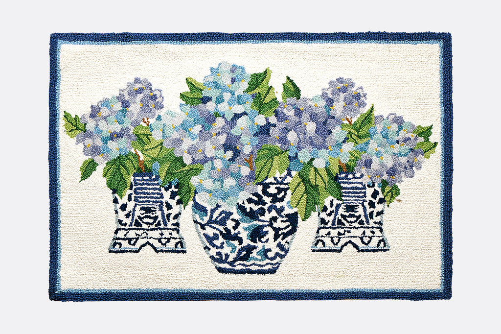 A blue and white hooked rug with illustrations of 3 vases with blue flowers with green leaves.