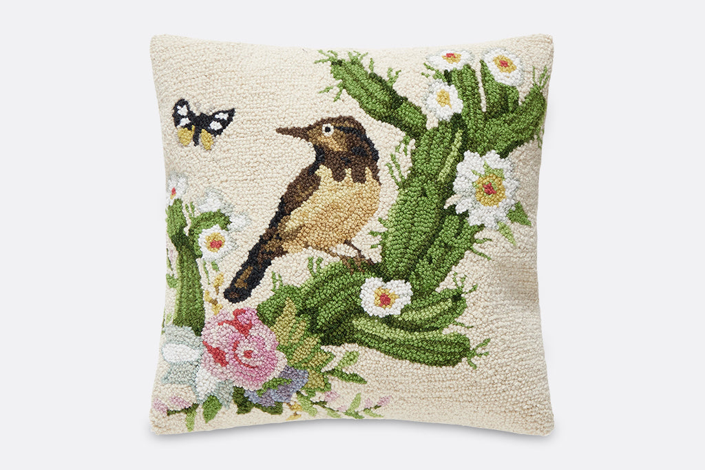 A hooked pillow of a green cactus with flowers, a bird, and a butterfly.
