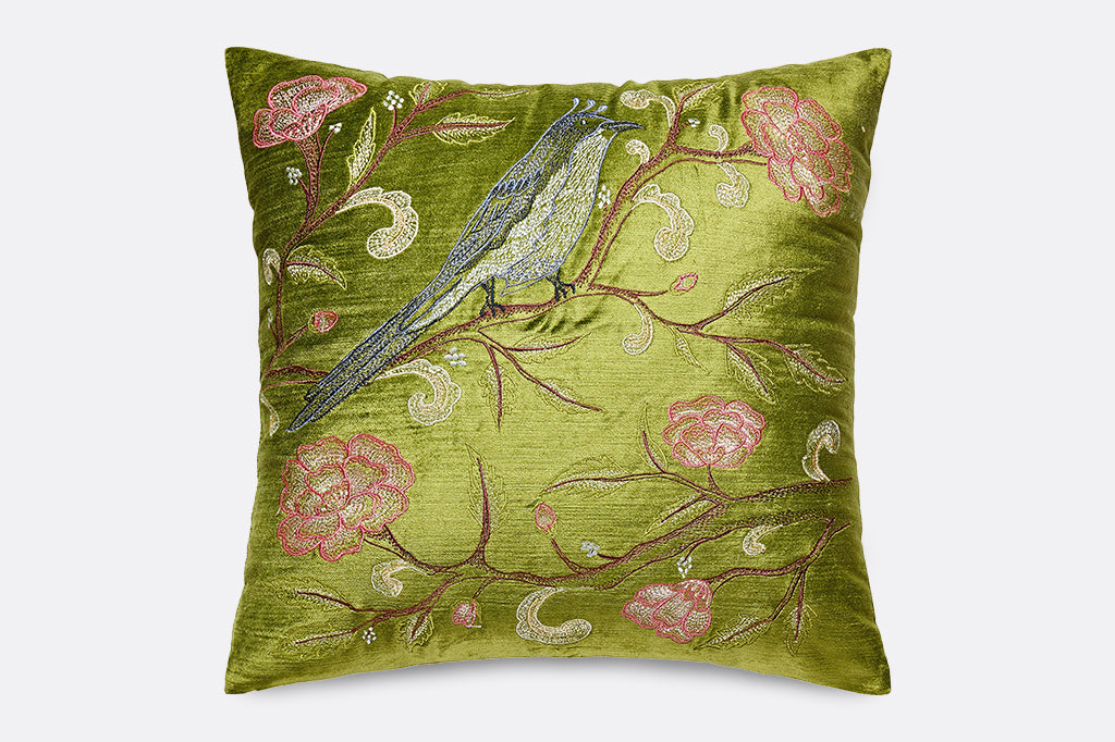 A green pillow with illustrations of a bird on a branch covered in flowers.