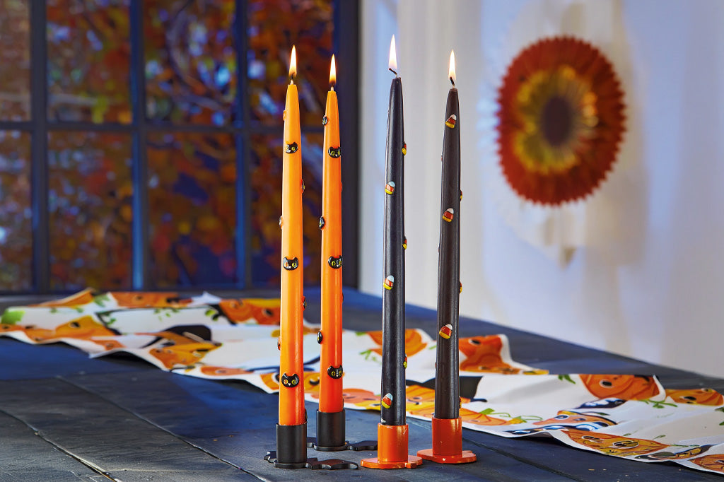 Four Halloween-themed candles on a table with decorative paper in the background.
