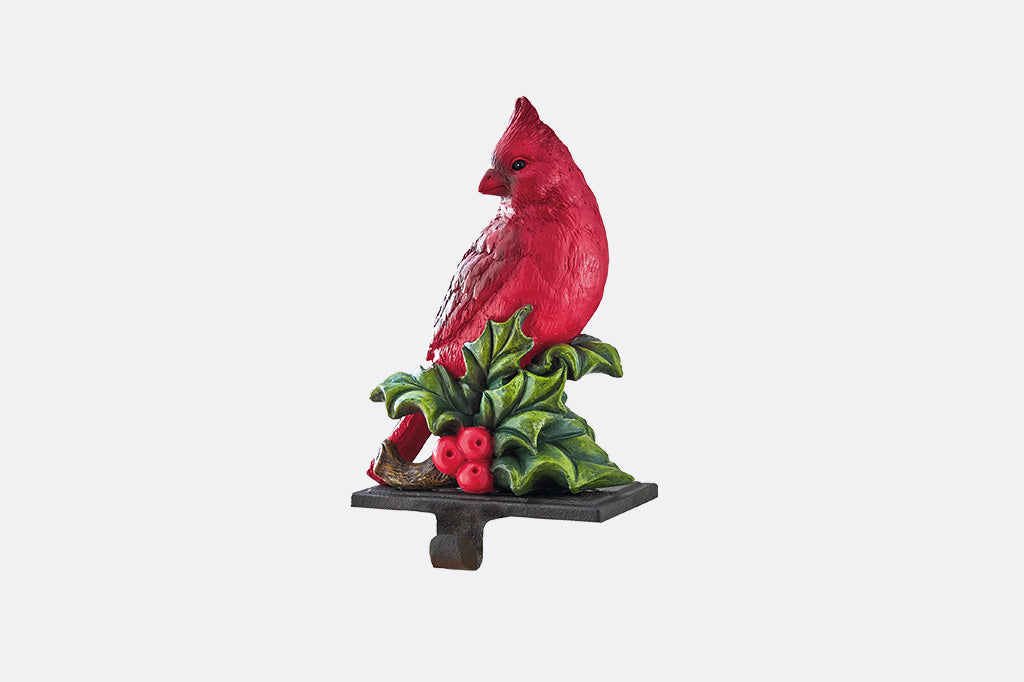 A decorative cardinal sculptured stocking hook perched on a holly branch with red berries, mounted on a dark rectangular base against a light gray background.