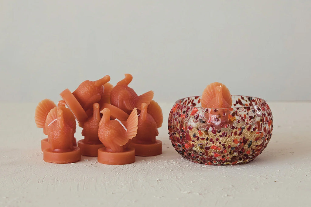 Set of orange bird-shaped candles with a decorative bowl on a light background
