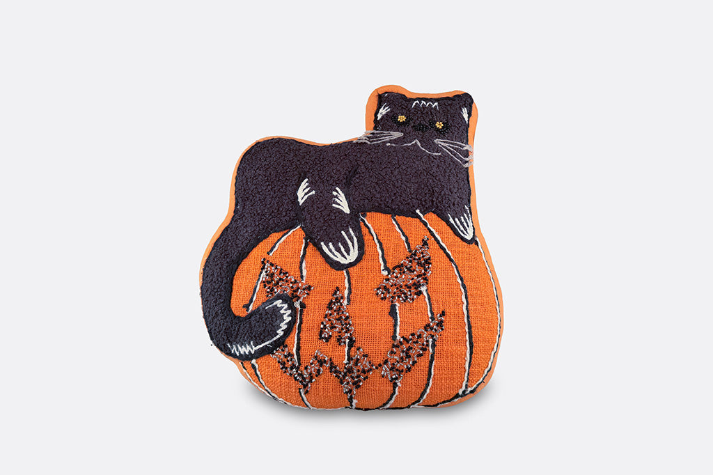 An orange jack o lantern shaped pillow with a black cat on top.