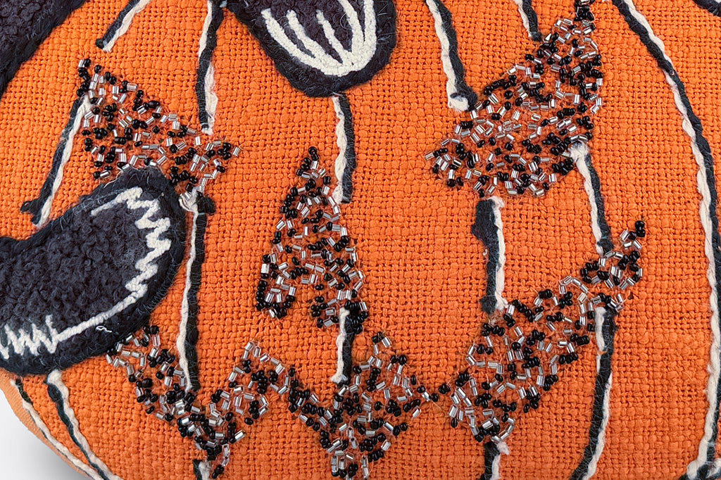 An orange jack o lantern shaped pillow with a black cat on top.