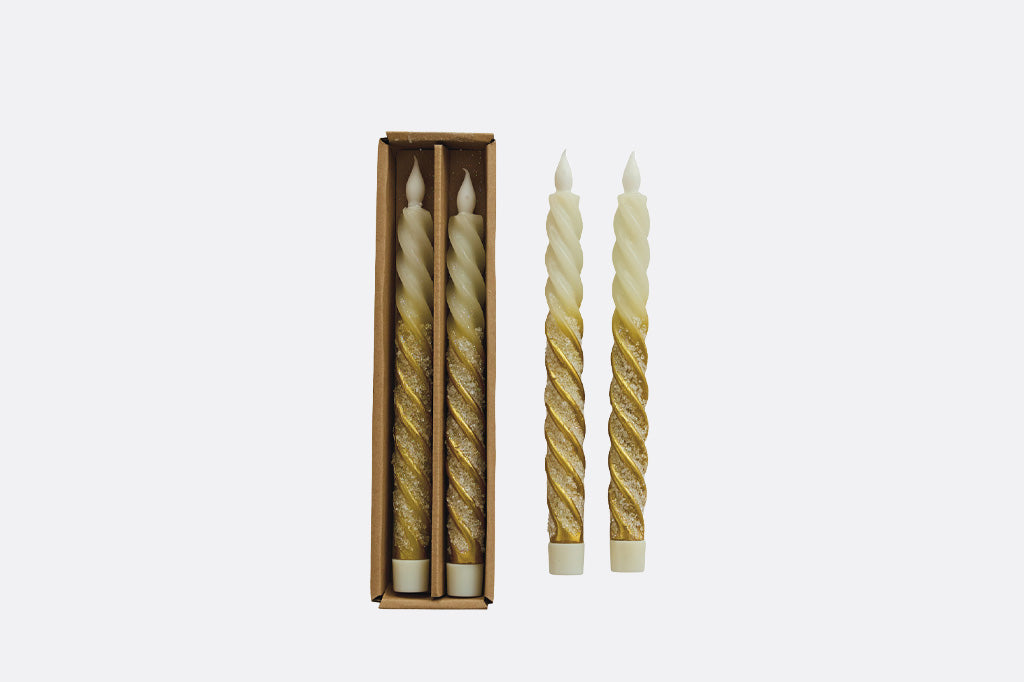 Two spiral flameless candles in packaging pictured next to two more  flameless candles with cream top coloring that melts into gold 