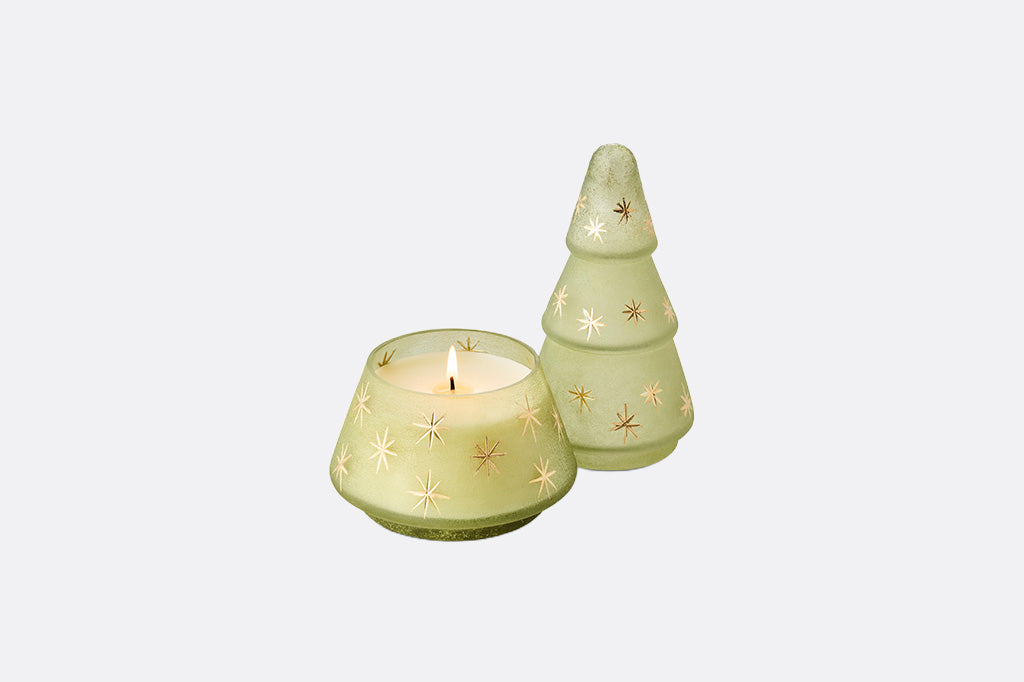 A light green candle holder set featuring a small tree-shaped candle holder with gold star cutouts and a matching shallow candle cup, both shown with a lit candle on a light gray background.