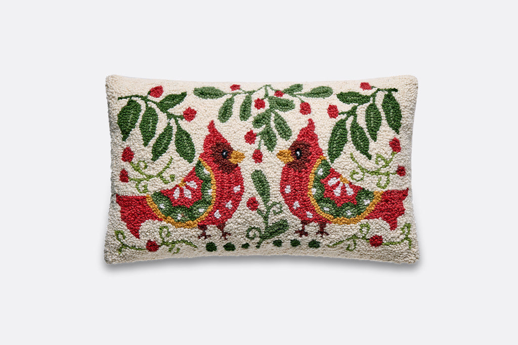 A rectangular hand-hooked throw pillow featuring two red cardinals under green leafy branches with red berries on a cream background.