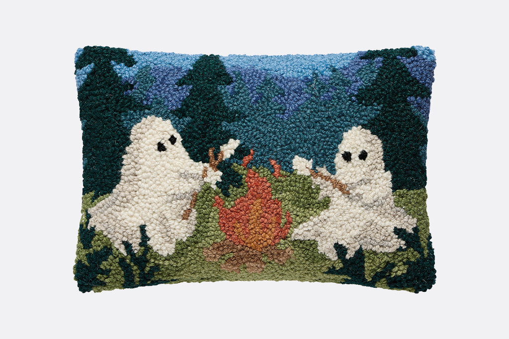 Decorative pillow with ghost design on a grassy field with trees and a blue sky.