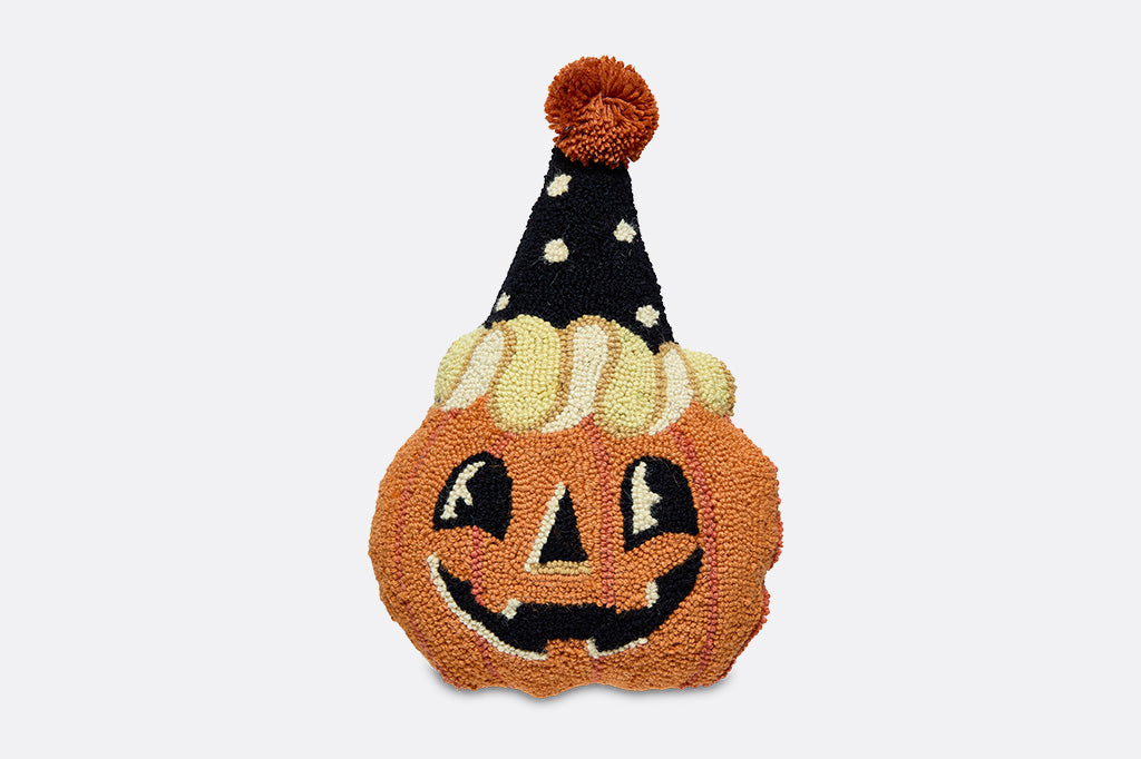 A pillow shaped like a jack-o-lantern with a party hat on.