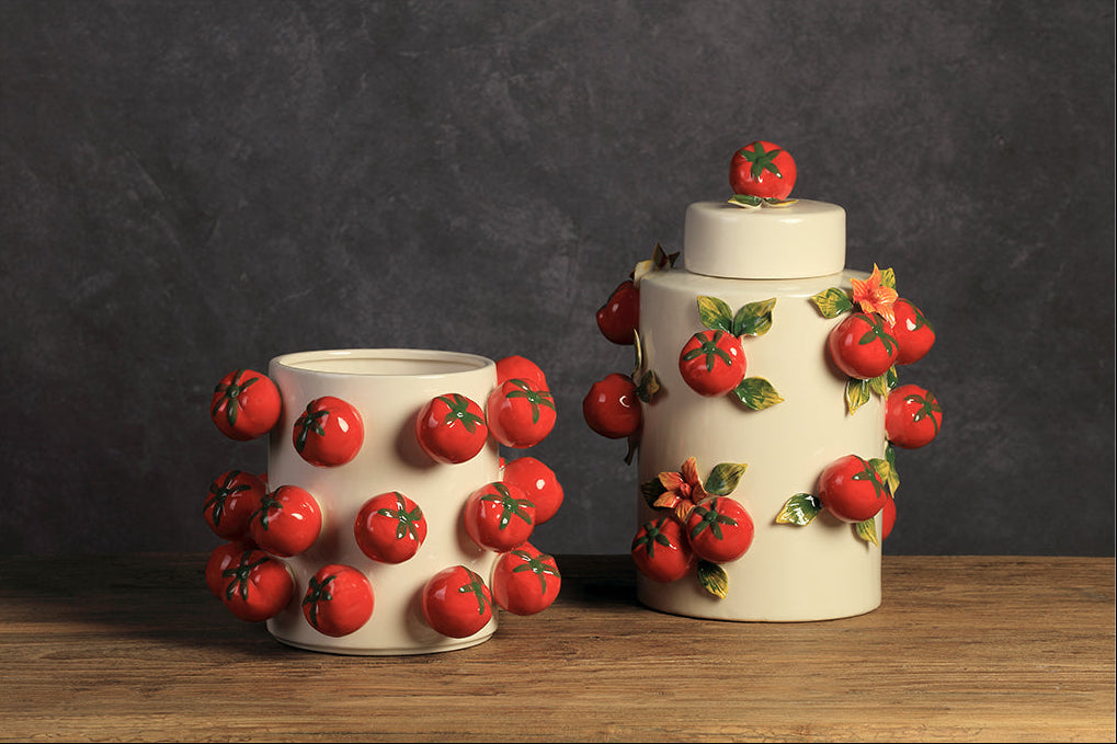 Two ceramic containers with tomato decorations on a wooden surface and dark background