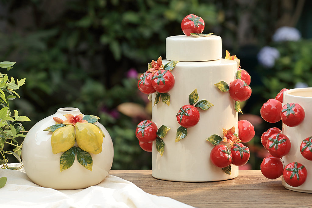 Ceramic jars with tomato and lemon designs on a wooden surface with a blurred natural background.
