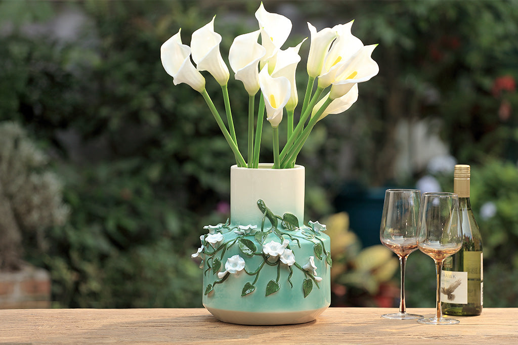 A vase with a green colorway and a design of vines and blossoming flowers.