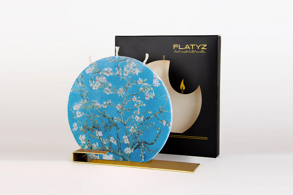 Round flat candle with three wick and a floral design on a stand next to a black box labeled 'FLATYZ'.