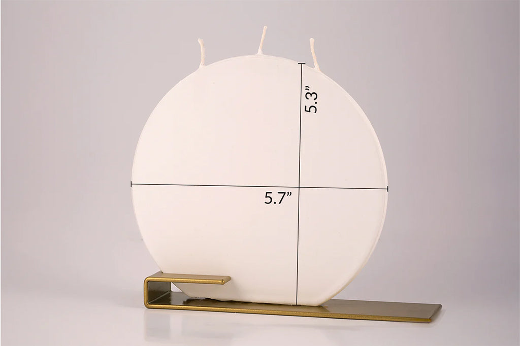 White flat circular candle with measurements on a gray background. 5.3"high and 5.7"wide. shown in golden steel holder