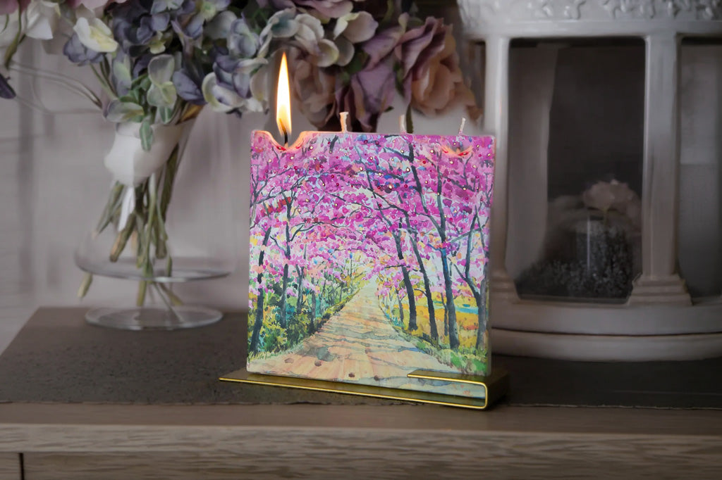 Decorative candle with a colorful forest design on a wooden surface.