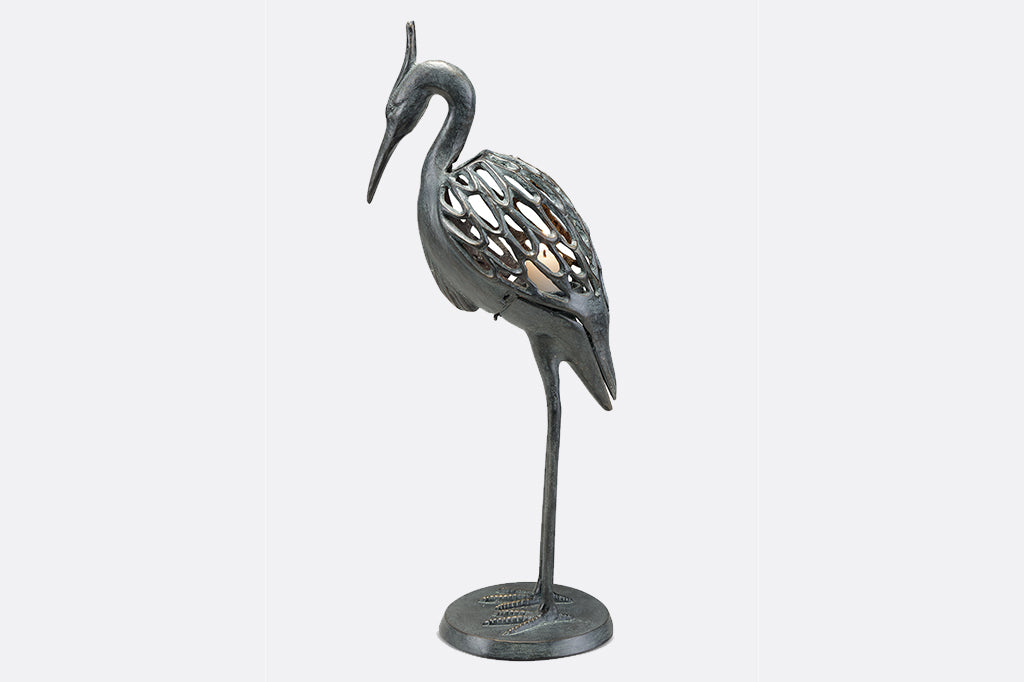 Modern metal heron candleholder with white lit candle  face left 