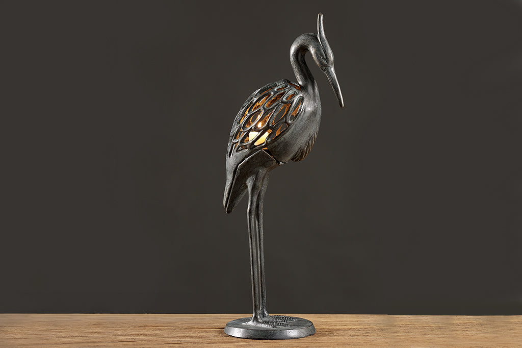 Modern metal heron candleholder with white lit candle  face right 