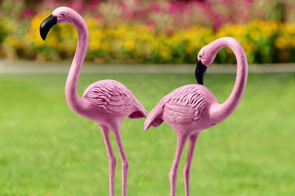 two cast metal pink flamingos in a garden, close-up view of their black beacks and pink feather details