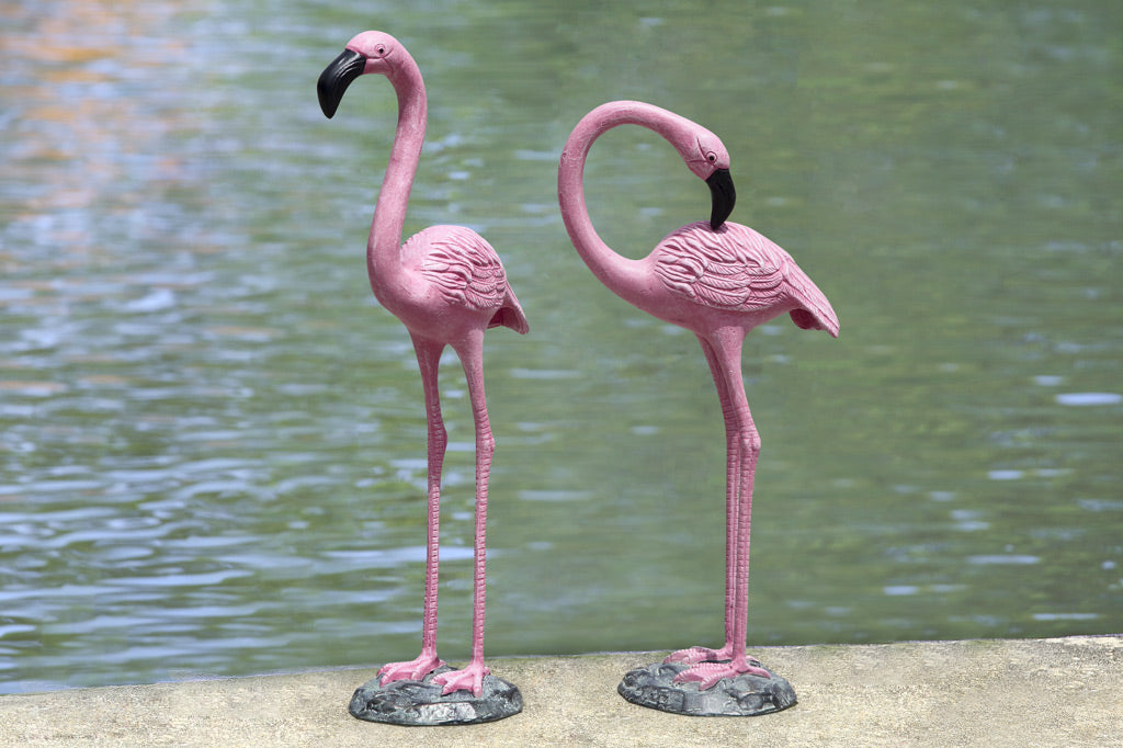 two cast metal pink flamingos on a shoreline