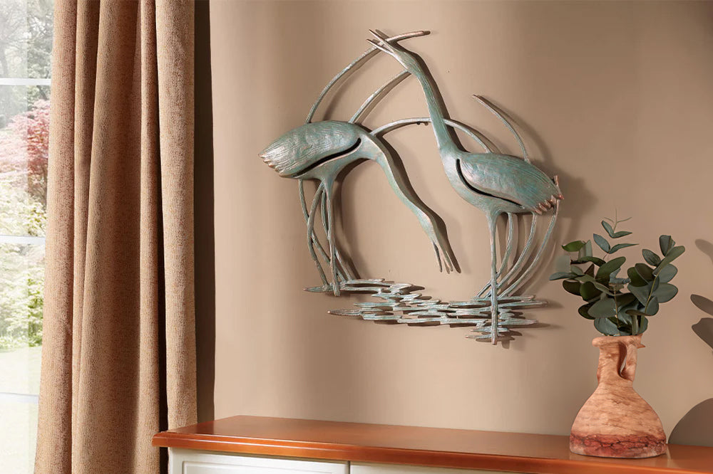 Wall plaque of two cranes standing in reeds and water shown above bedroom dresser by vase of eucalyptus