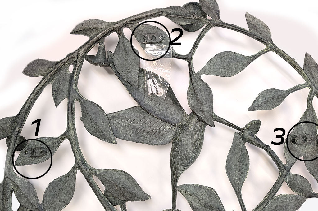 Decorative metal wall art with leaf patterns and numbered circles highlightingthe three hanging hardware locations