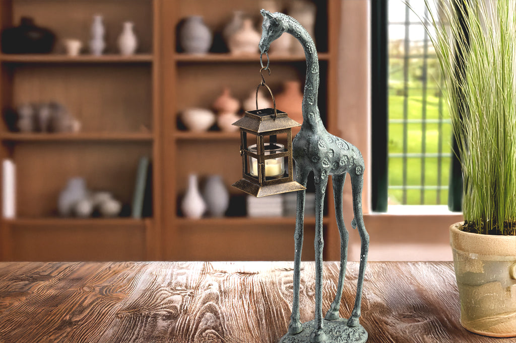 cast metal giraffe holding lantern in mouth sculpture  shown on desk in living room/home office setting