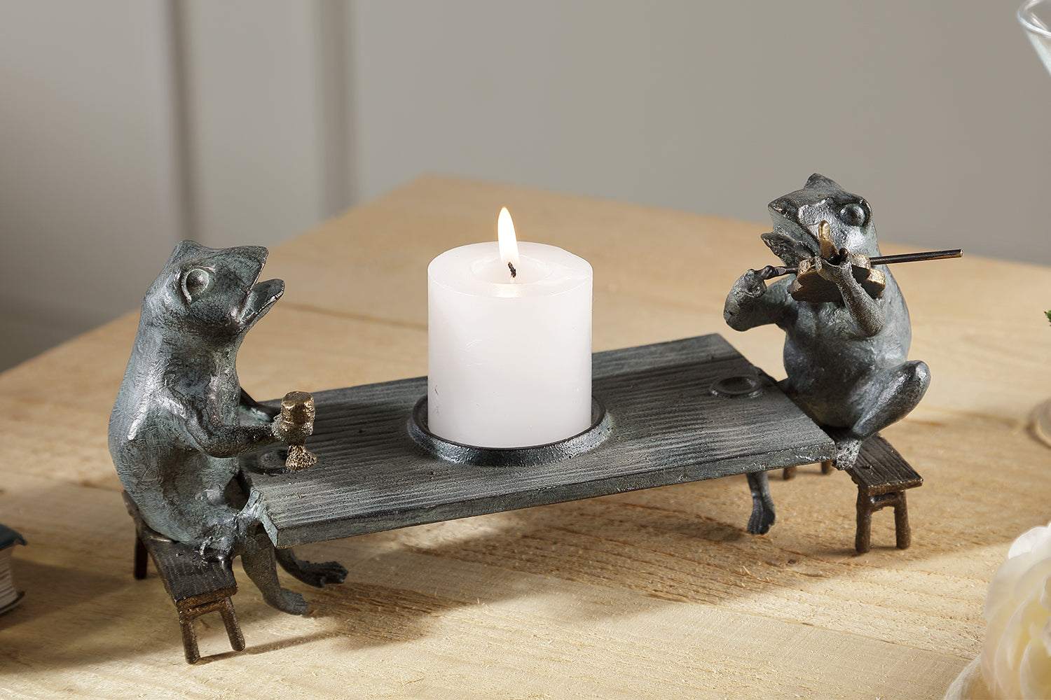 table top candleholder shaped like two frogs at a table; one holds cup and the other serenades by playing a violin