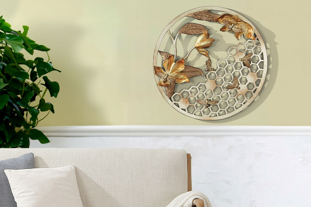 Circular wall plaque in golden cast metal finish featuring bees, honeycomb and blossoms shown on wall above couch and near houseplant