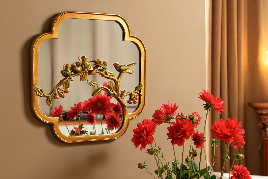 Chinoiserie mirror with golden and green birds on a branch hung on a wall over a dresser with red flowers
