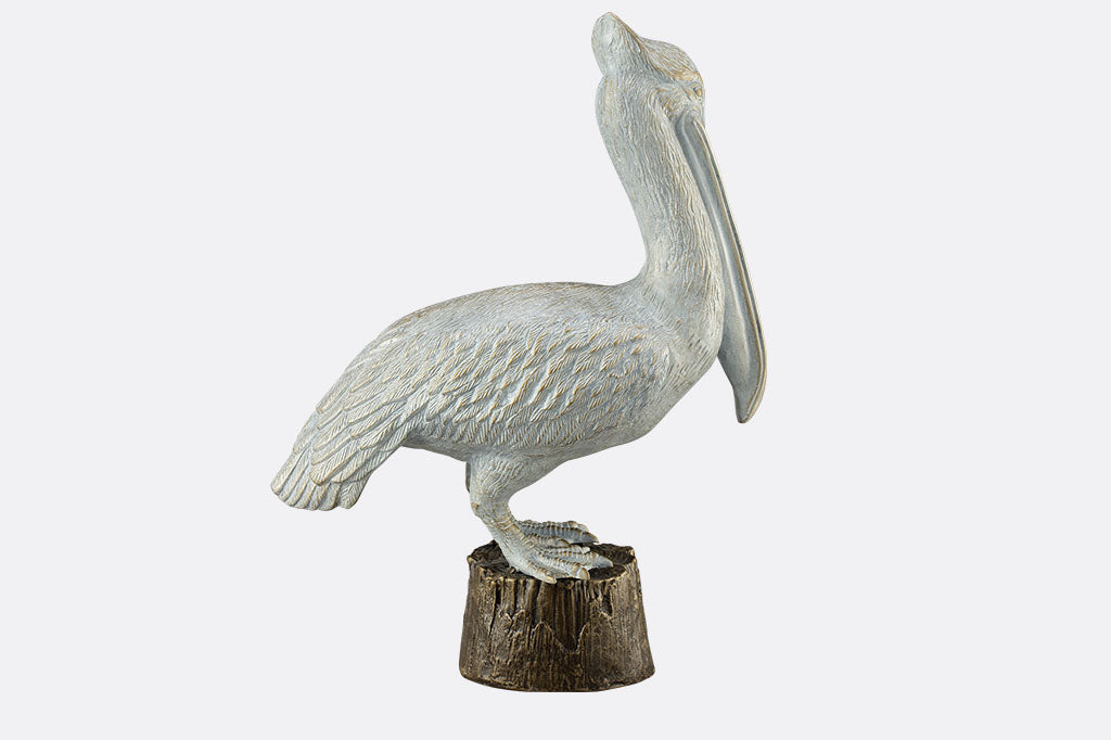 Aluminum garden sculpture of  white pelican standing upon a pier piling.  Shown face-right