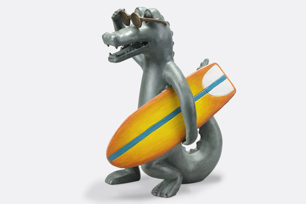 Alligator garden sculpture with sunglasses holding a orange and yellow surf board